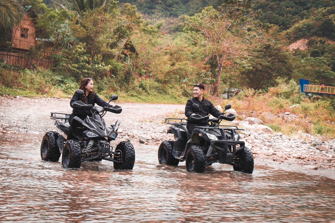 services-01 Two people enjoy an exciting quad biking adventure through a scenic river landscape.