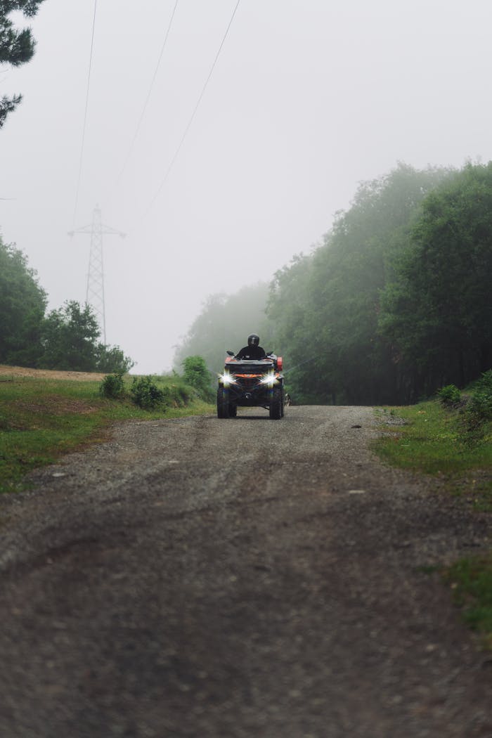 A lone ATV rider navigating a foggy dirt path through a lush forest.