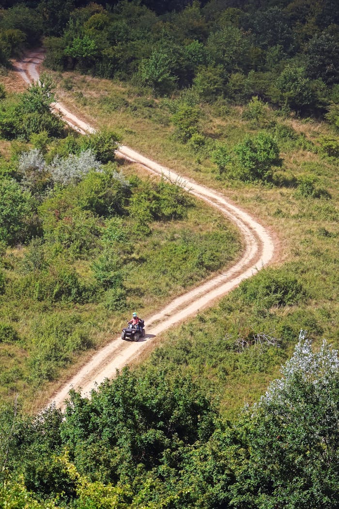 services-03 Rider navigating an all-terrain vehicle on a winding dirt road through lush greenery in Hungary.